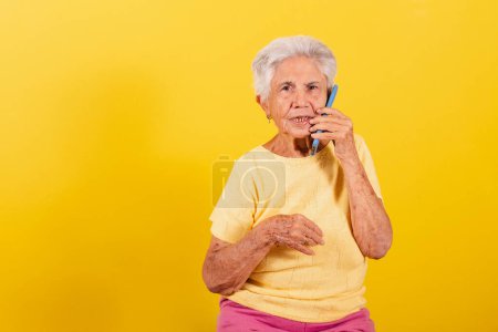 Photo for Old lady, holding cell phone, inclusion of the elderly in the digital environment, online, smartphone. Talking by voice call. - Royalty Free Image