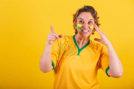 Foto de Mujer adulta adulta, aficionado al fútbol brasileño, apuntando algo a la distancia, foto publicitaria. - Imagen libre de derechos