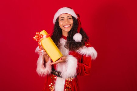 Photo for Beautiful brazilian black woman, dressed as santa claus, christmas clothes. holding yellow gift. - Royalty Free Image