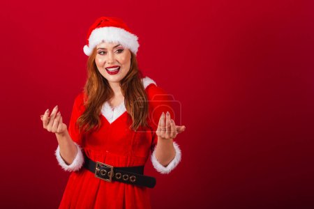 Foto de Hermosa brasileña pelirroja, vestida con ropa de Navidad, Santa Claus. invitando a las manos. - Imagen libre de derechos