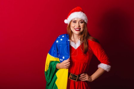 Photo for Beautiful Brazilian red-haired woman, dressed in Christmas clothes, Santa Claus. holding brazil flag. - Royalty Free Image