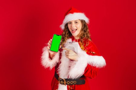 Photo for Brazilian woman, dressed in Santa Claus outfit, holding smartphone with green screen in Chroma. - Royalty Free Image
