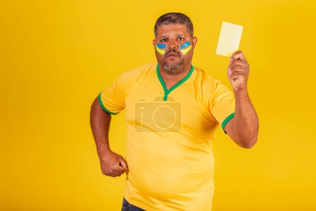 Foto de Hombre negro brasileño, fanático del fútbol de Brasil. mostrando tarjeta amarilla. falta de - Imagen libre de derechos