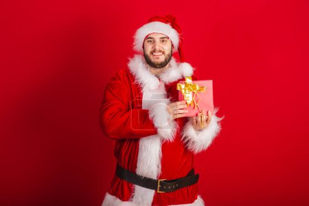 Photo for Caucasian, Brazilian man dressed in Christmas outfit, Santa Claus. holding red gift. - Royalty Free Image