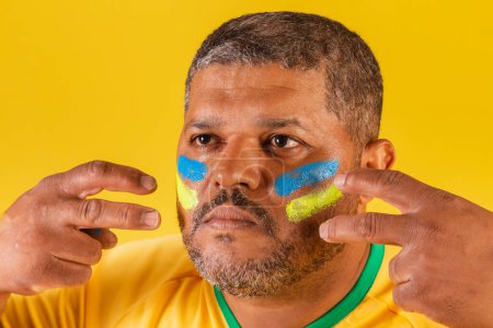 Foto de Hombre negro brasileño, fanático del fútbol de Brasil. foto de cerca, la aplicación de pintura facial, preparándose para el partido, la competencia. - Imagen libre de derechos