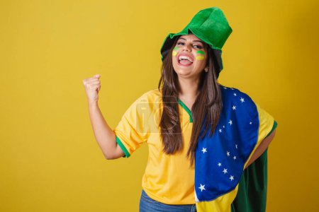 Photo for Woman supporter of Brazil, world cup 2022, wearing typical fan outfit to go to the game, brazil flag and green hat. partying. - Royalty Free Image