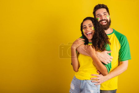Téléchargez les photos : Couple de supporters brésiliens de football, vêtus aux couleurs de la nation, femme noire, homme caucasien. ensemble, romantique - en image libre de droit