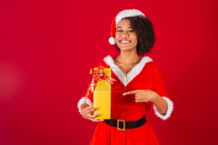 Téléchargez les photos : Belle femme brésilienne noire, habillée en Père Noël claus, maman claus, pointant vers le cadeau - en image libre de droit