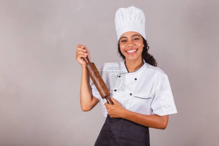 Téléchargez les photos : Jeune Brésilienne noire, cuisinière. Roulette en bois pour préparer pâtes, pizza et pain. - en image libre de droit