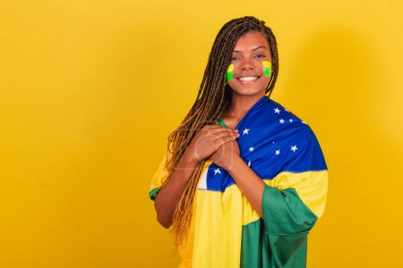 Foto de Mujer negra joven aficionada al fútbol brasileño. usando la bandera, cantando himno nace. - Imagen libre de derechos