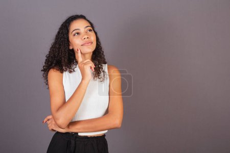 Téléchargez les photos : Jeune femme noire brésilienne, doigt sur le menton, réfléchissant. - en image libre de droit