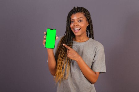 Téléchargez les photos : Jeune femme afro brésilienne montrant écran de smartphone. espace pour publicités, applications, mobiles. - en image libre de droit