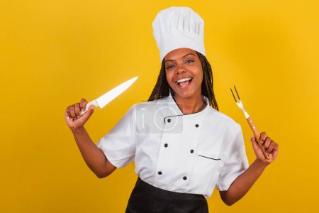 Photo for Young afro brazilian woman, chef cook, holding knife and fork for barbecue, getting ready to cook. - Royalty Free Image