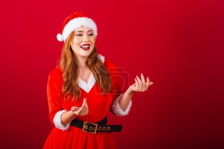 Photo for Beautiful Brazilian red-haired woman, dressed in Christmas clothes, Santa Claus. inviting hands. - Royalty Free Image