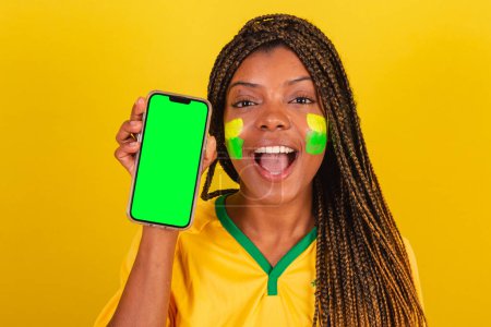 Téléchargez les photos : Femme noire jeune fan de football brésilien. tenant un téléphone portable, une application, un smartphone. gros plan photo - en image libre de droit