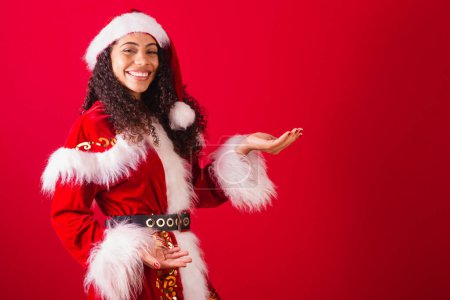 Téléchargez les photos : Belle femme noire brésilienne, habillée en Père Noël claus, vêtements de Noël. présentation du produit avec les mains. - en image libre de droit