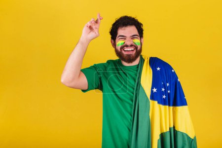 Foto de Hombre caucásico con barba, brasileño, fanático del fútbol de Brasil, dedos cruzados, deseando, tener suerte. Sorteo del premio. - Imagen libre de derechos