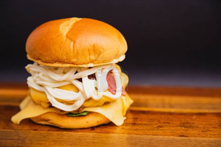 Téléchargez les photos : Délicieux hamburger de bœuf triple fait à la main avec fromage caillé, mozzarella et bacon frit. sur panneau en bois. - en image libre de droit
