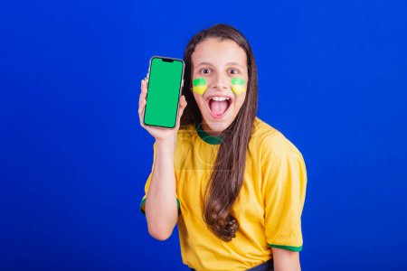 Foto de Jovencita, fanática del fútbol de Brasil. celebración de teléfono celular, pantalla para publicidad, promoción. Smartphone. solicitudes. - Imagen libre de derechos