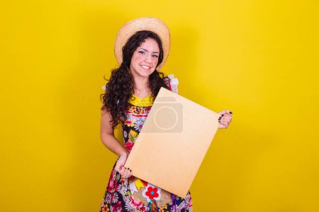 Photo for Beautiful woman dressed in typical clothes for a Festa Junina. holding sign for text or ad, advertisement. - Royalty Free Image