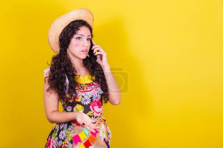 Téléchargez les photos : Belle femme vêtue de vêtements typiques pour une Festa Junina. parler par appel audio sur téléphone portable. - en image libre de droit