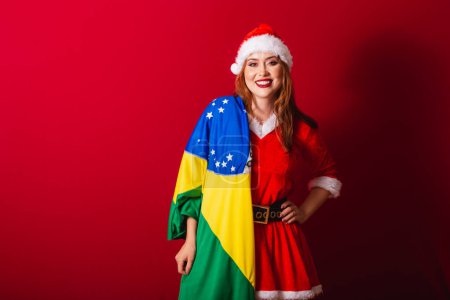 Foto de Hermosa brasileña pelirroja, vestida con ropa de Navidad, Santa Claus. sosteniendo bandera de Brasil. - Imagen libre de derechos