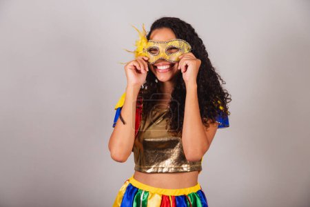 Foto de Hermosa mujer brasileña negra, con traje de frevo, y paraguas, carnaval. poner máscara de carnaval en la cara. - Imagen libre de derechos