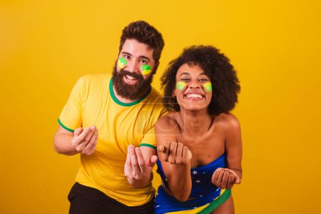 Téléchargez les photos : Couple de fans de football brésilien, habillé dans les couleurs du brésil, femme noire, homme caucasien. invitant les mains. appel, bienvenue - en image libre de droit