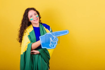 Photo for Woman soccer fan, fan of brazil, world cup, wearing foam glove. pointing to negative space, ad, text or advertising. Right side. - Royalty Free Image