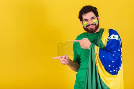 Téléchargez les photos : Homme caucasien avec barbe, brésilien, fan de football de brésil, pointage du doigt vers la gauche, photo pour la publicité, indication. - en image libre de droit