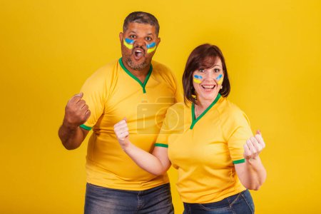 Photo for Couple, red-haired woman and black man, Brazilian soccer fans. celebrating. - Royalty Free Image