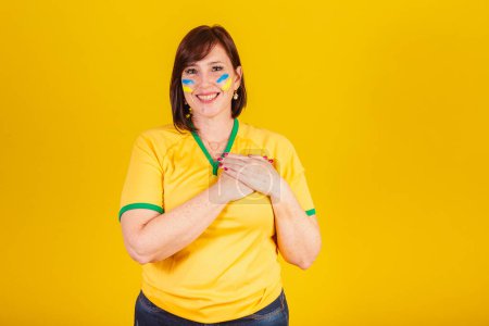 Foto de Mujer pelirroja, fan del fútbol brasileño. Con las manos en el pecho, gratitud. - Imagen libre de derechos