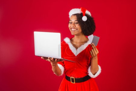 Téléchargez les photos : Belle femme brésilienne noire, habillée en Père Noël claus, maman claus, tenant cartes de crédit et carnet - en image libre de droit