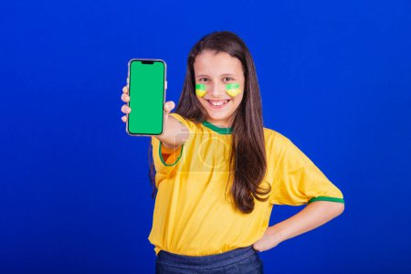 Téléchargez les photos : Jeune fille, fan de football du Brésil. tenant le téléphone portable, écran pour la publicité, promotion. Smartphone. applications. - en image libre de droit