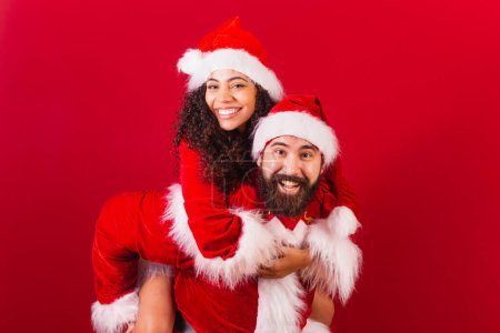 Photo for Brazilian couple, dressed for christmas, santa claus, mummy claus. playing together, hugging. approved, black woman and caucasian man. - Royalty Free Image