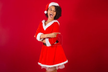 Photo for Beautiful black brazilian woman, dressed as santa claus, mama claus, presenting product or information on the side - Royalty Free Image