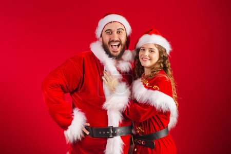 Photo for Brazilian couple, dressed in Christmas clothes, Santa Claus, hugging, giving kiss - Royalty Free Image