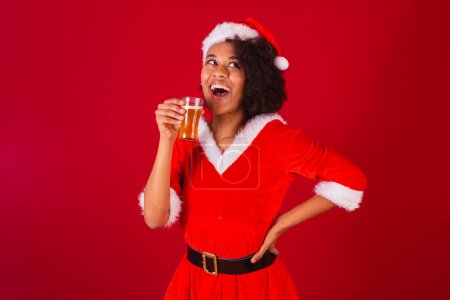 Téléchargez les photos : Belle femme brésilienne noire, habillée comme Santa Claus, maman Claus, boire de la bière - en image libre de droit