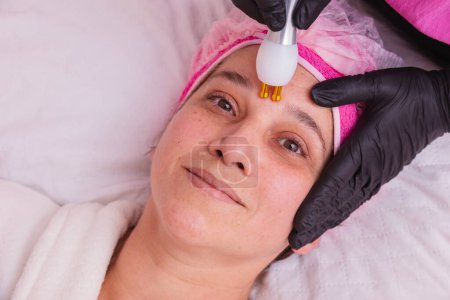 Téléchargez les photos : Belle femme adulte. faire un traitement facial avec jet de plasma dans une clinique de beauté. - en image libre de droit