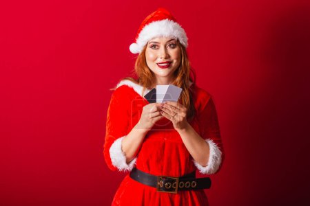Photo for Beautiful Brazilian red-haired woman, dressed in Christmas clothes, Santa Claus. holding credit cards. - Royalty Free Image