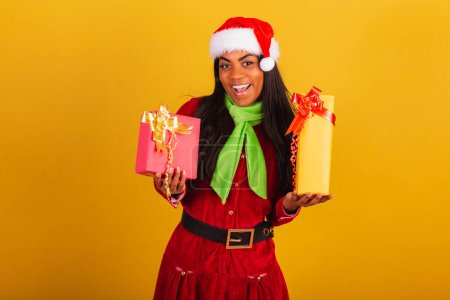 Photo for Beautiful black Brazilian woman, dressed in Christmas clothes, Santa Claus, holding two gifts. - Royalty Free Image