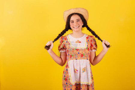 Foto de Chica vestida con ropa naranja tradicional para festa junina. Sujetando trenzas para el cabello, sonriendo. - Imagen libre de derechos
