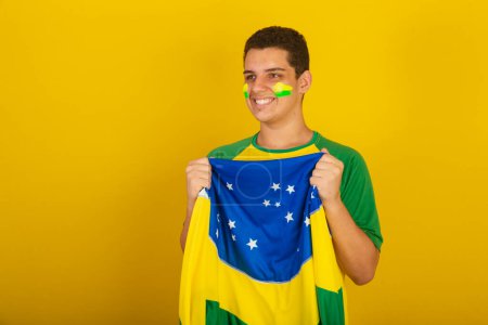 Téléchargez les photos : Jeune Brésilien fan de foot. habillé en vert, flottant avec le drapeau brésilien. - en image libre de droit
