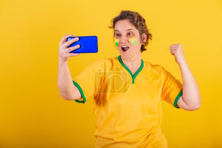 Téléchargez les photos : Adulte femme adulte, fan de football brésilien, smartphone, regarder match de football par téléphone portable, streaming. - en image libre de droit