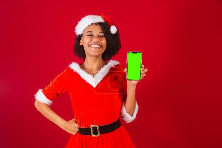 Photo for Beautiful black brazilian woman, dressed as santa claus, mama claus, showing smartphone screen - Royalty Free Image