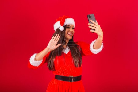Téléchargez les photos : Belle Brésilienne vêtue de vêtements de Noël, le Père Noël. tenant smartphone prenant autoportrait. - en image libre de droit