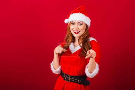 Photo for Beautiful Brazilian red-haired woman, dressed in Christmas clothes, Santa Claus. pointing at camera, choosing you. - Royalty Free Image