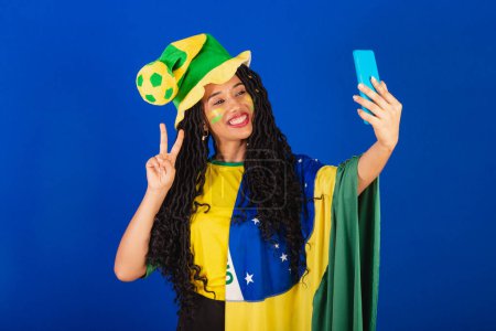 Téléchargez les photos : Jeune Brésilien noir, fan de foot. autoportrait en selfie, smartphone. - en image libre de droit