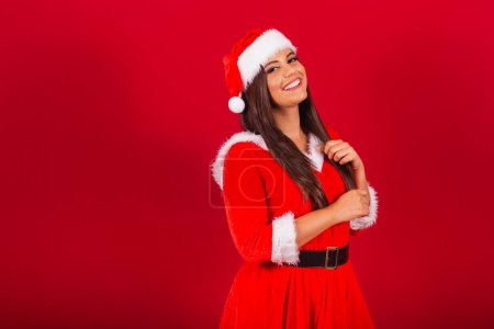 Téléchargez les photos : Belle Brésilienne vêtue de vêtements de Noël, le Père Noël. tenant dans les cheveux. - en image libre de droit