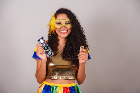 Photo for Beautiful black Brazilian woman, with frevo clothes, carnival. wearing a mask, holding a condom, fight against hiv, aids. - Royalty Free Image